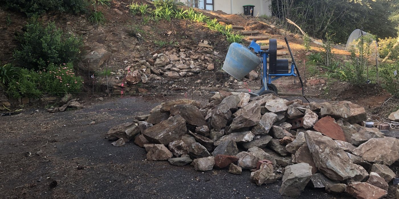 Cleared rubble pile and cement mixer at the base of the sloped site during retaining wall construction in Glen Osmond