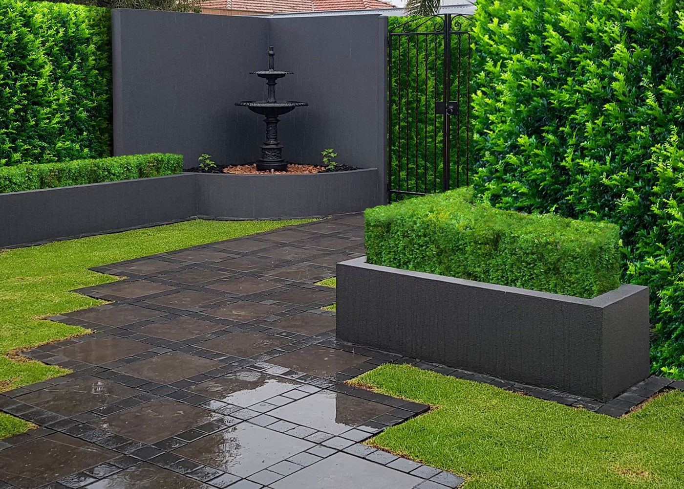 Finished courtyard garden in Glenelg with a metal fountain, rendered planter walls, hedging and slate paving