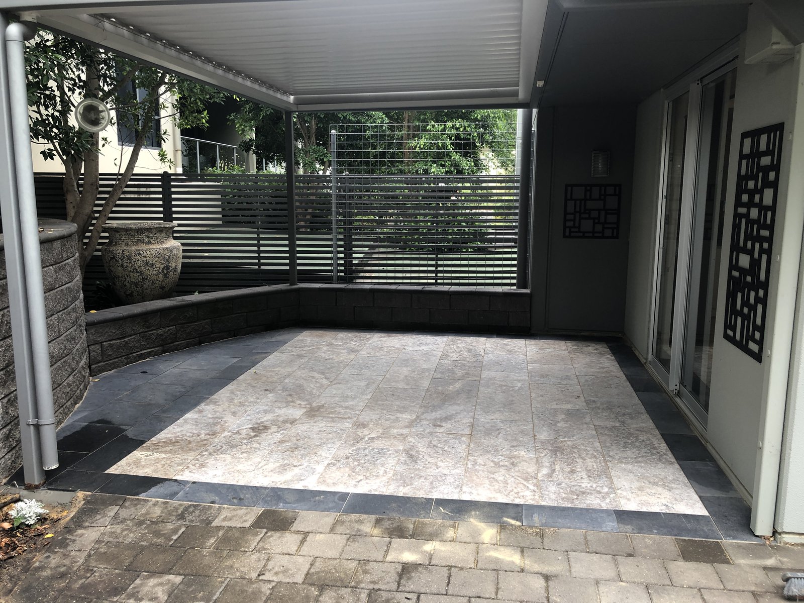 Travertine paved alfresco entertaining area under a covered patio, bordered with a dark slate edge and a rendered retaining wall