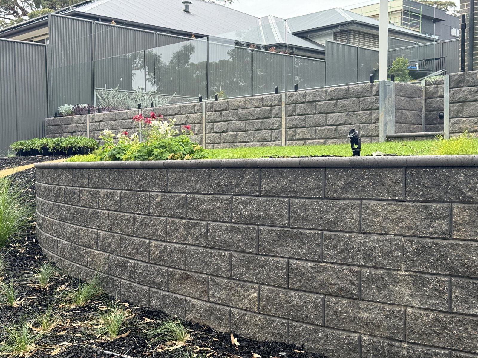 Curved concrete block retaining wall with bullnose coping below a glass pool fence in Craigburn Farm