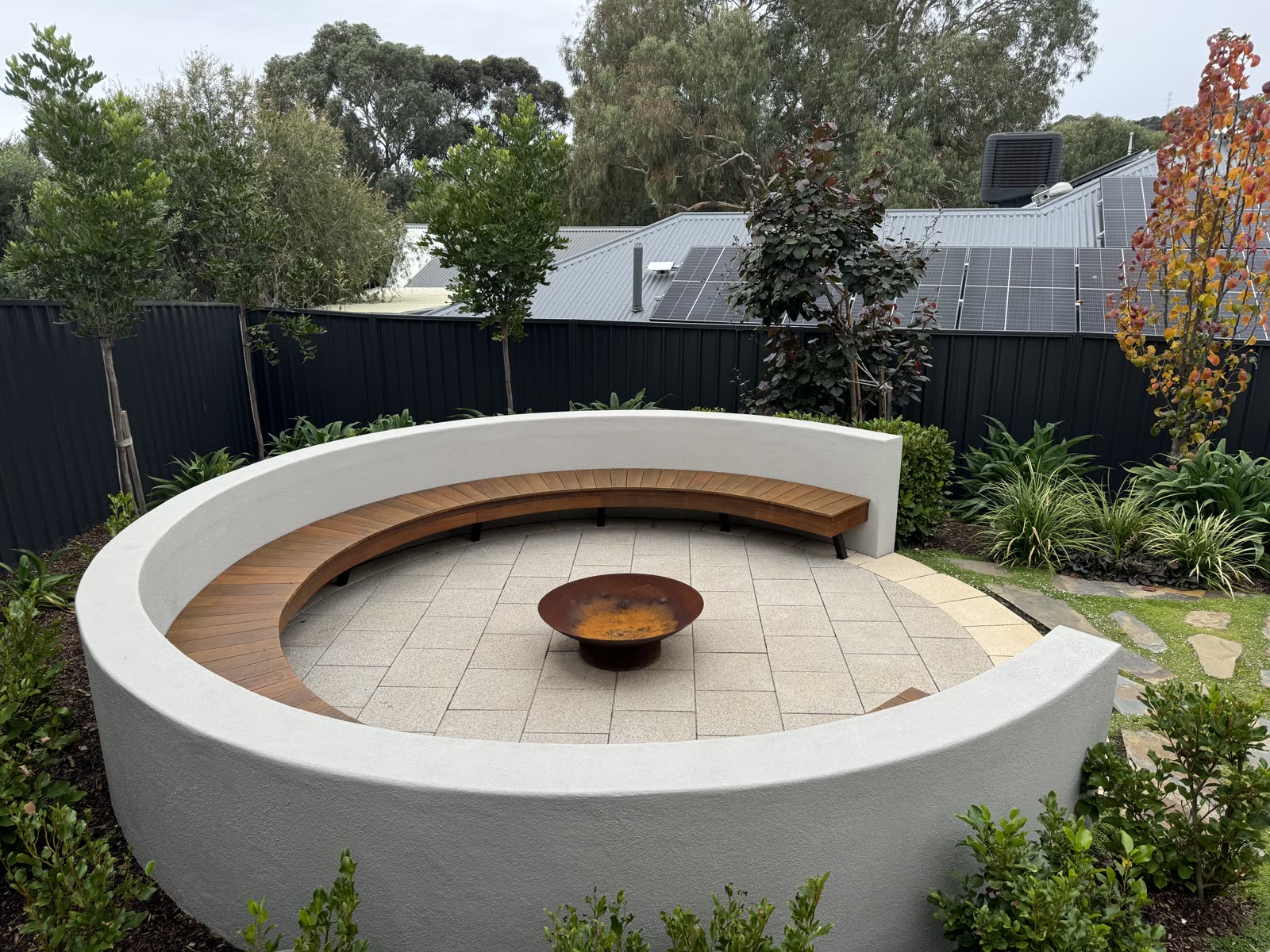 Circular rendered fire pit feature with a curved built-in timber bench in Aberfoyle Park