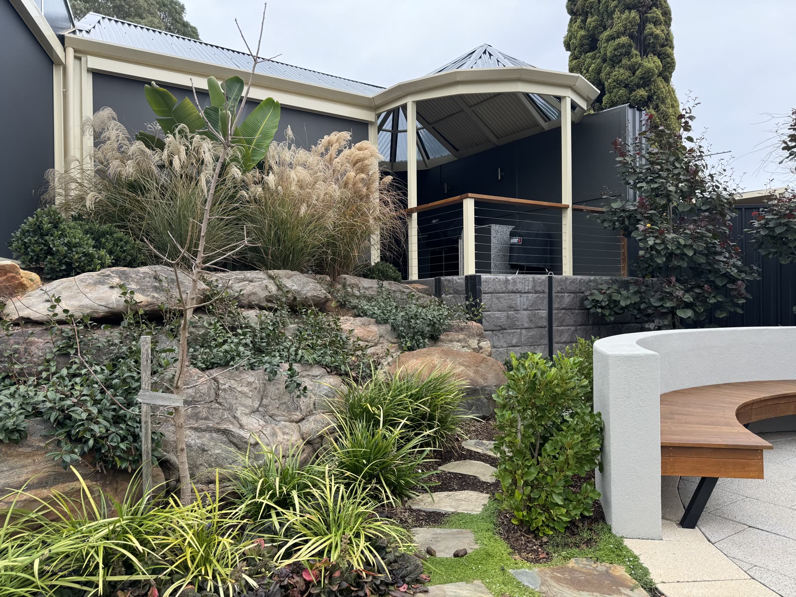 Terraced sloping backyard in Aberfoyle Park with a boulder retaining feature, curved white rendered bench and a gazebo entertaining area