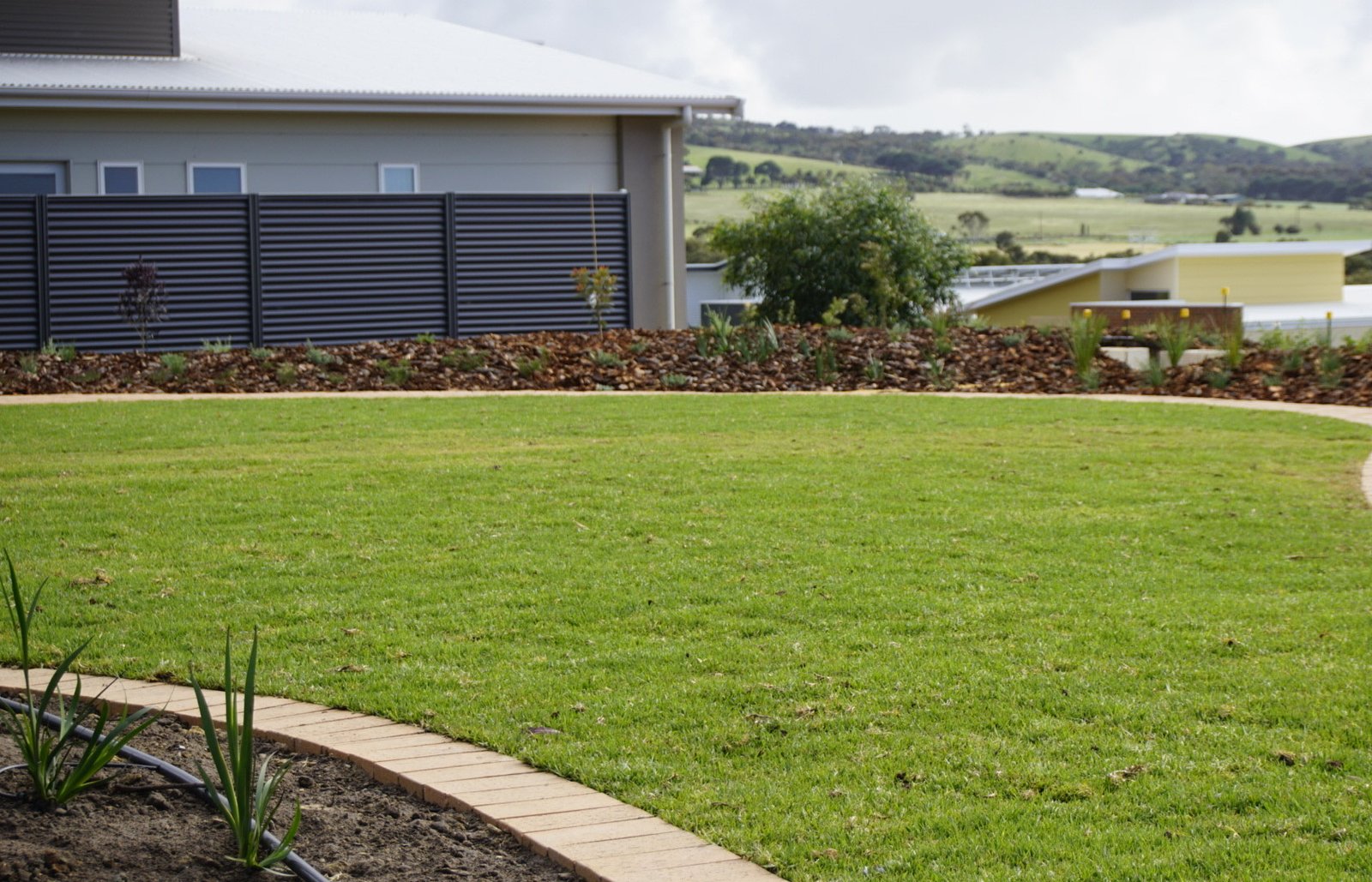 New circular front lawn with mulched garden beds and a paved path in Chiton, overlooking rural hills