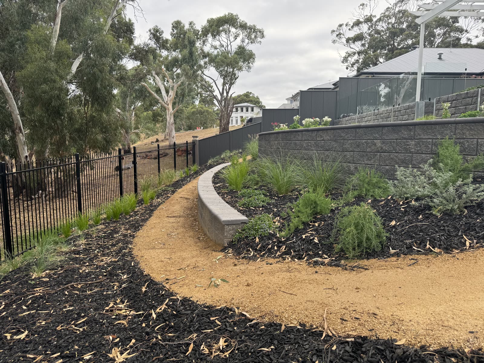 Curved gravel path lined with native tussock grasses and low-maintenance planting along a segmental retaining wall in Craigburn Farm