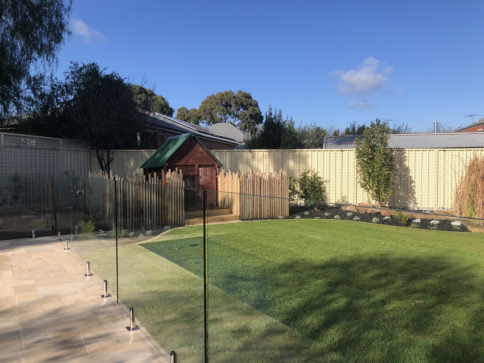 Finished backyard renovation in Evandale with a curved lawn, frameless glass pool fence, new garden beds and a rebuilt cubby house