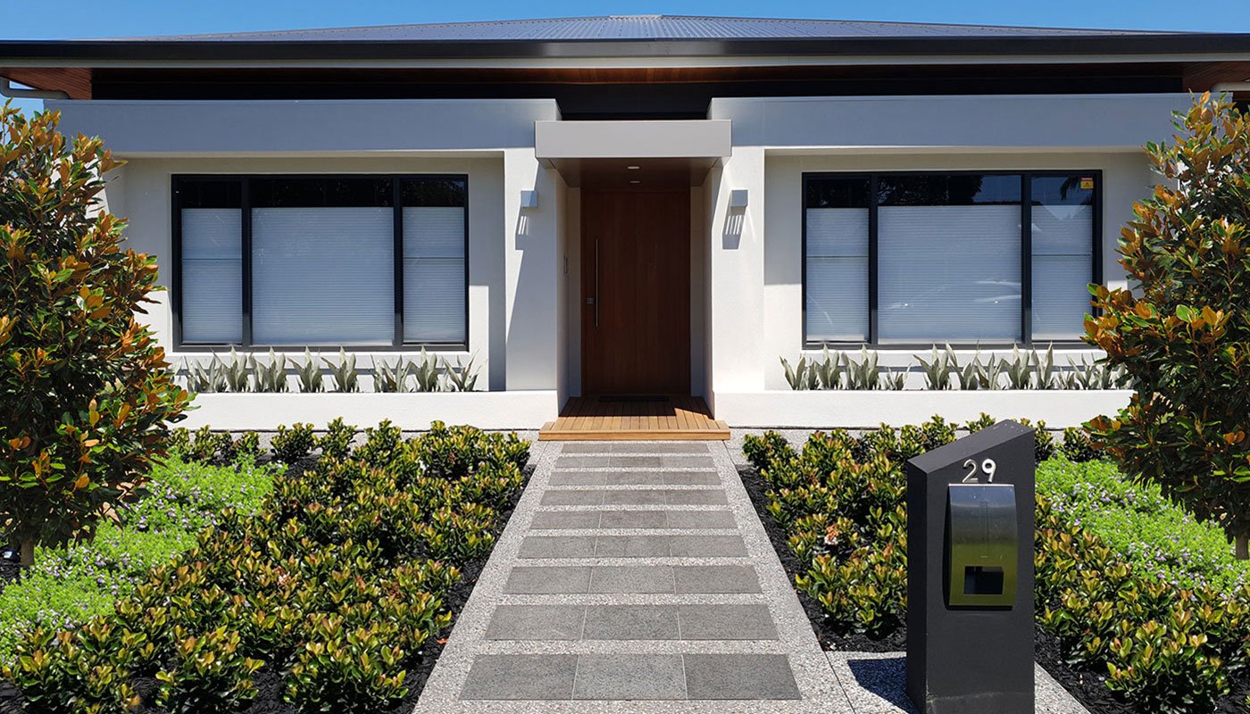 Modern front garden with a magnolia hedge, native strappy planting and a granite paver path leading to the front door