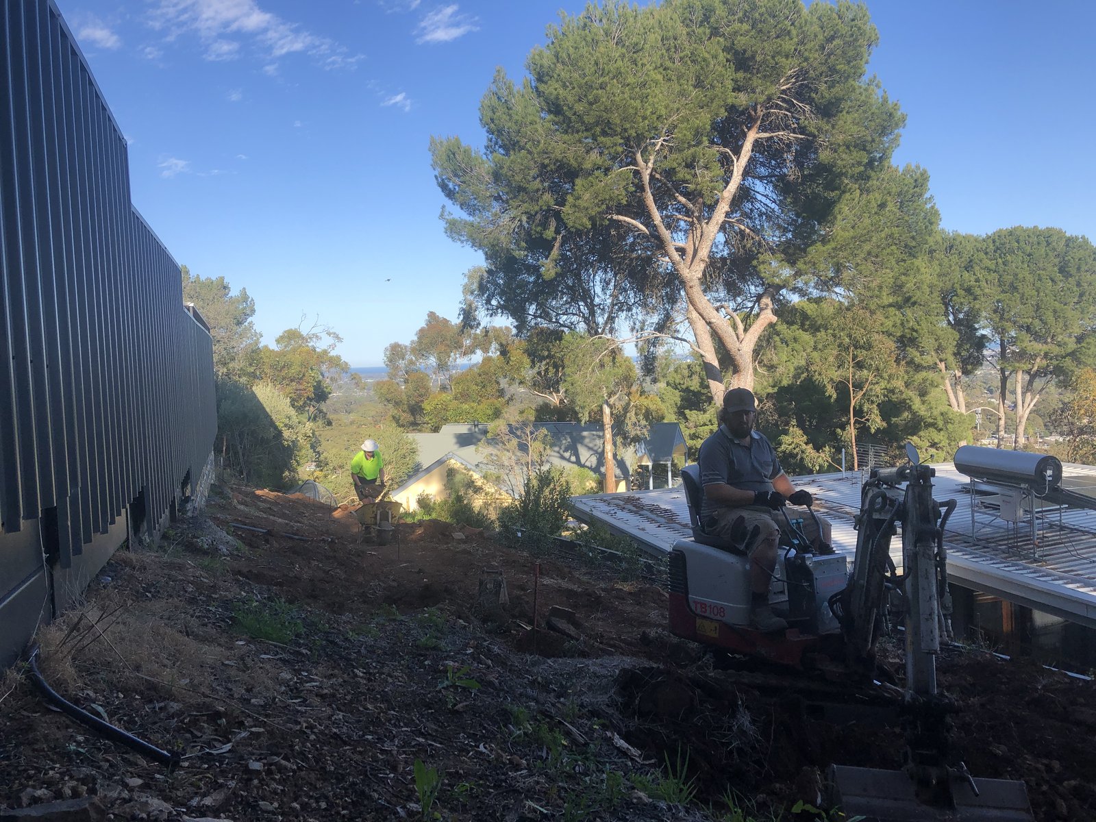 Mini excavator and drilling rig working a steep sloping block during earthworks in Glen Osmond