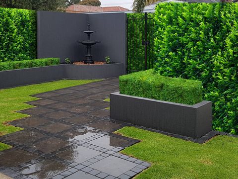Dark charcoal grid-pattern pavers set into lawn leading to a tiered fountain in a Glenelg North courtyard, framed by clipped hedging