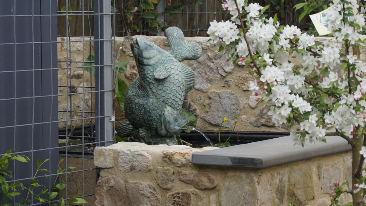 Bronze fish water feature spouting into a sandstone-walled pond in McLaren Vale