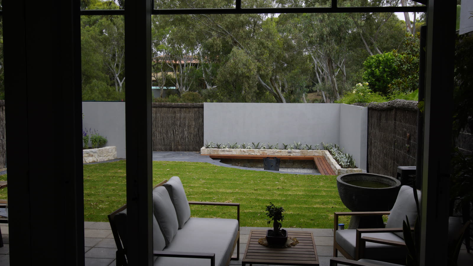 Sunken outdoor entertaining area in St Peters with a rendered feature wall, sandstone-capped bench seating, firepit and lawn