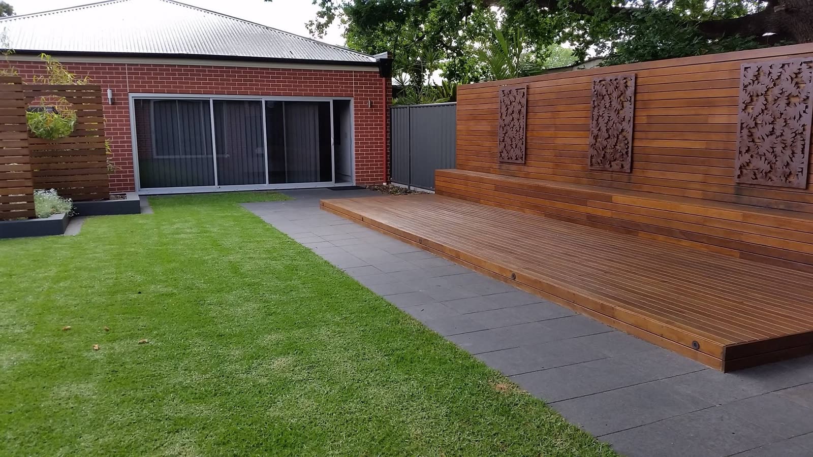 Hardwood timber deck and matching feature wall with decorative laser-cut timber panels, alongside new lawn and paving